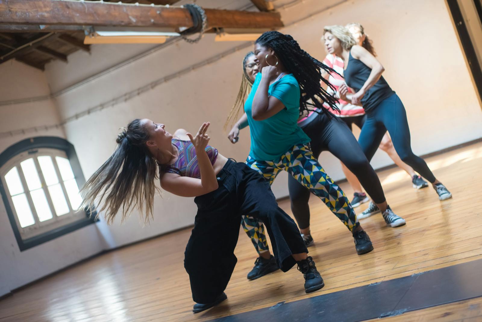 Women engage in a lively dance class in a well-lit studio, enjoying movement and skill.
